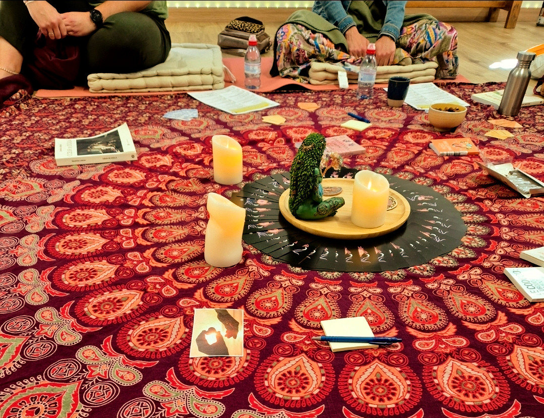 Cercle d'atelier vu de près : grand tissu à mandala, plateau de bois avec bougies et statuette au centre, carnets, ouvrages et gourdes autour