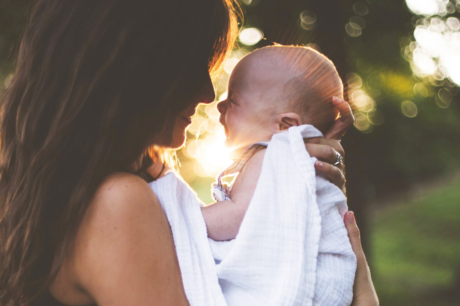 Une femme tient son nouveau-né face à elle, à contre-jour devant une lumière dorée