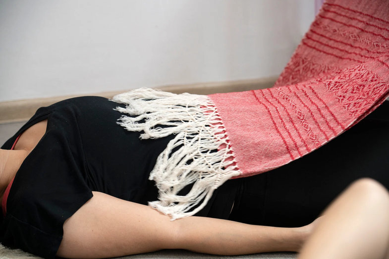 Une personne allongée sur le côté, un rebozo rouge à franges blanches posé sur sa hanche