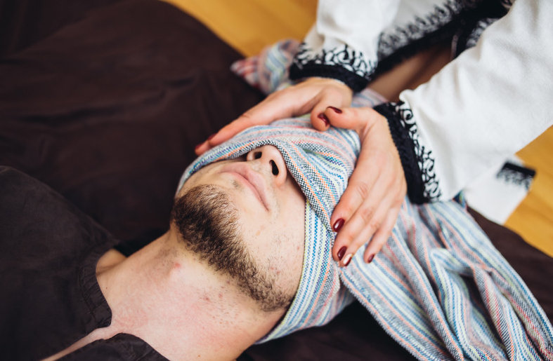Un homme allongé, un rebozo rayé posé sur ses yeux, les mains de la praticienne par-dessus