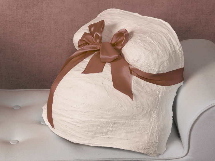 Moulage de ventre de grossesse en plâtre blanc, ceint d'un ruban de satin rose noué en nœud, posé sur un fauteuil clair