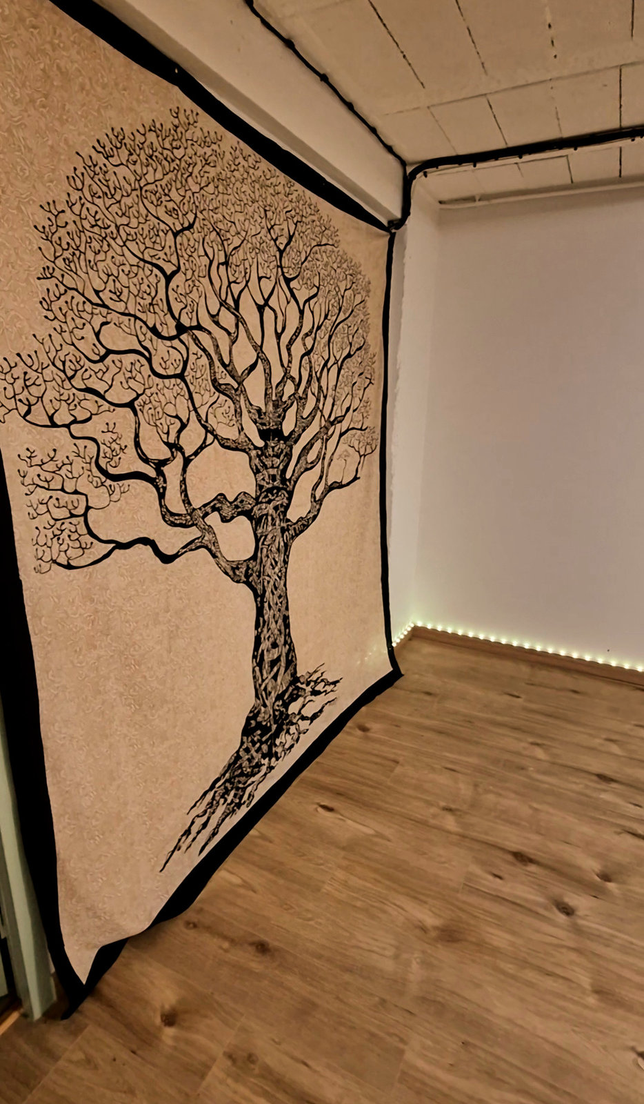 Salle d'atelier : une grande tenture imprimée d'un arbre de vie noir sur fond écru couvre le mur, parquet clair et ruban lumineux le long de la plinthe